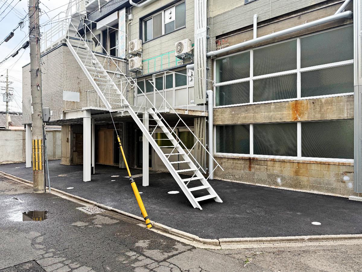 京都市下京区朱雀宝蔵町56の賃貸物件/外観。白い階段を上がって二階の引戸を開けると共用ラウンジにつながっています。2階左手に飛び出しているのが冷蔵室部分