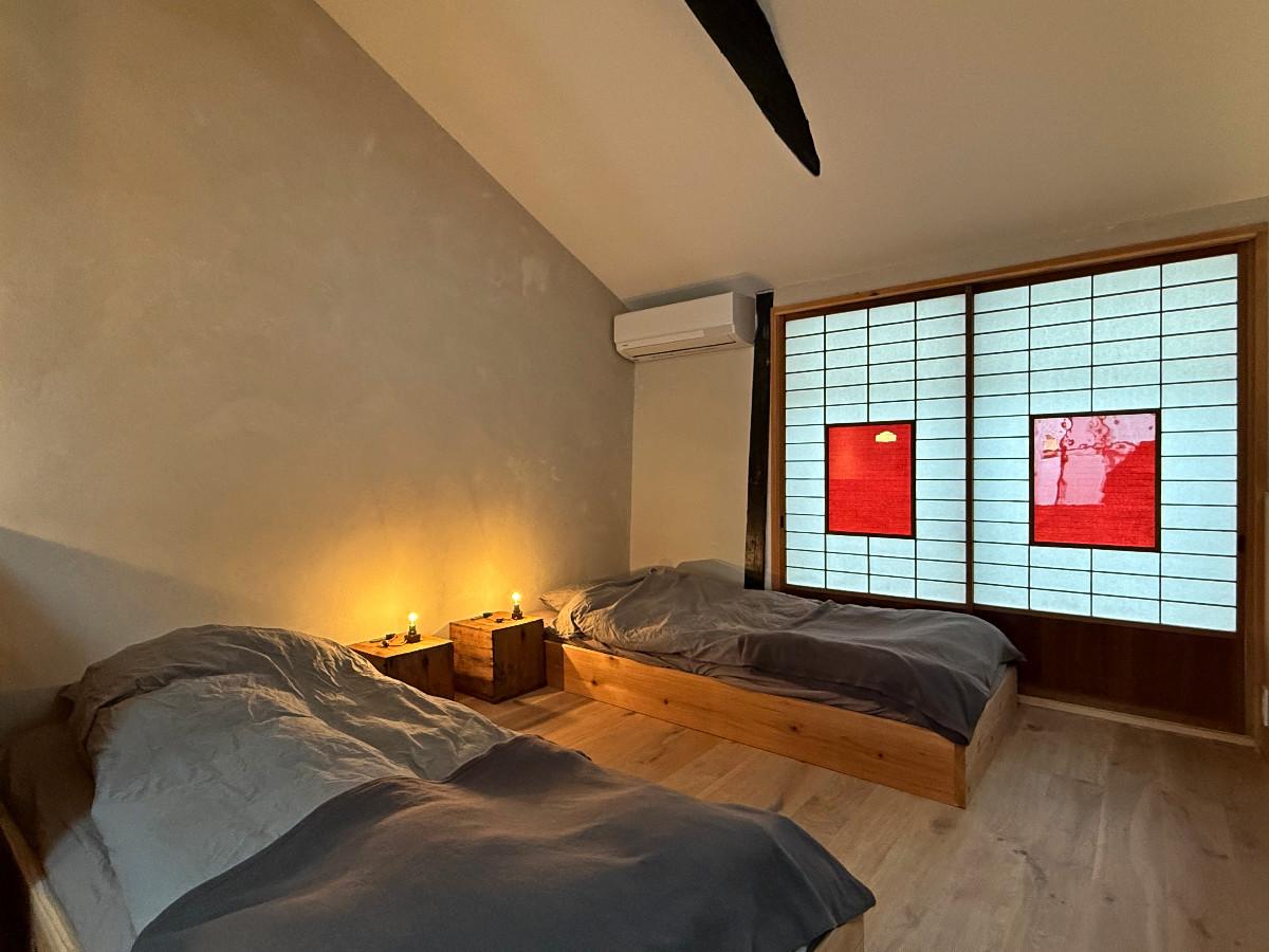 〒600-8141 京都府京都市下京区新日吉町の賃貸物件/2階ベッドコーナー。町屋ですので、低めベッドでお布団風に。サイドテーブルにオリジナル照明がきらりと光ります。建具の赤もポップで日本人にはない感覚