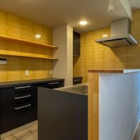 埼玉県入間市仏子の売買物件/キッチン本体はブラックで引き締めて。マスタードイエローのタイルとのコントラストも素敵。腰壁はちょっとしたカウンターとして使える木の天板が乗っています