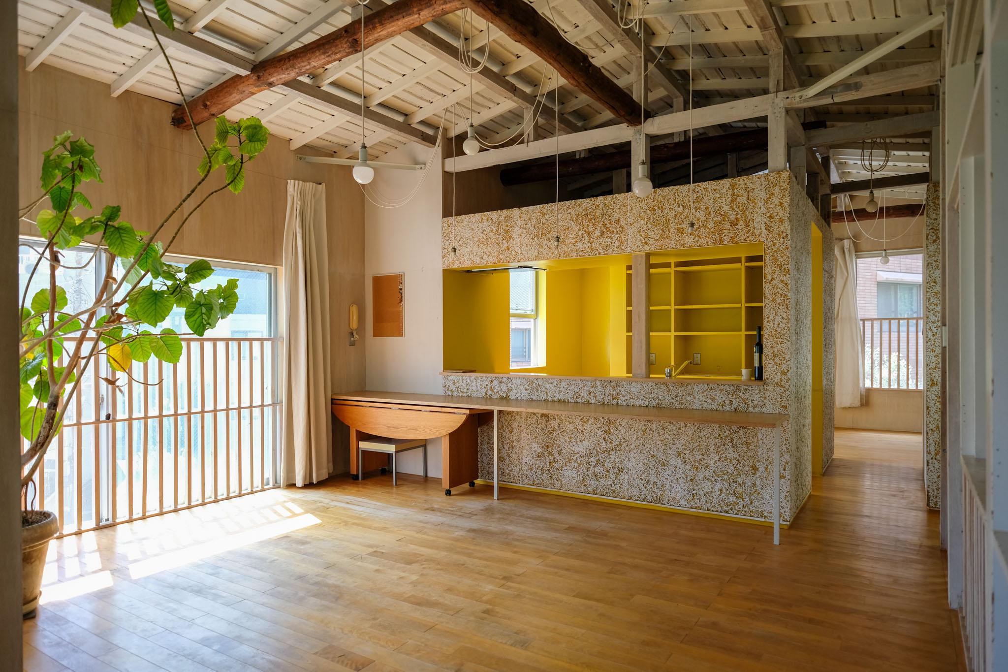 文京区白山の賃貸物件/開放的な2階リビング。印象的な梁を残した小屋組みの白く塗装された天井に、ざっくりと黄色に塗装された木毛セメント板の「箱」がポイント