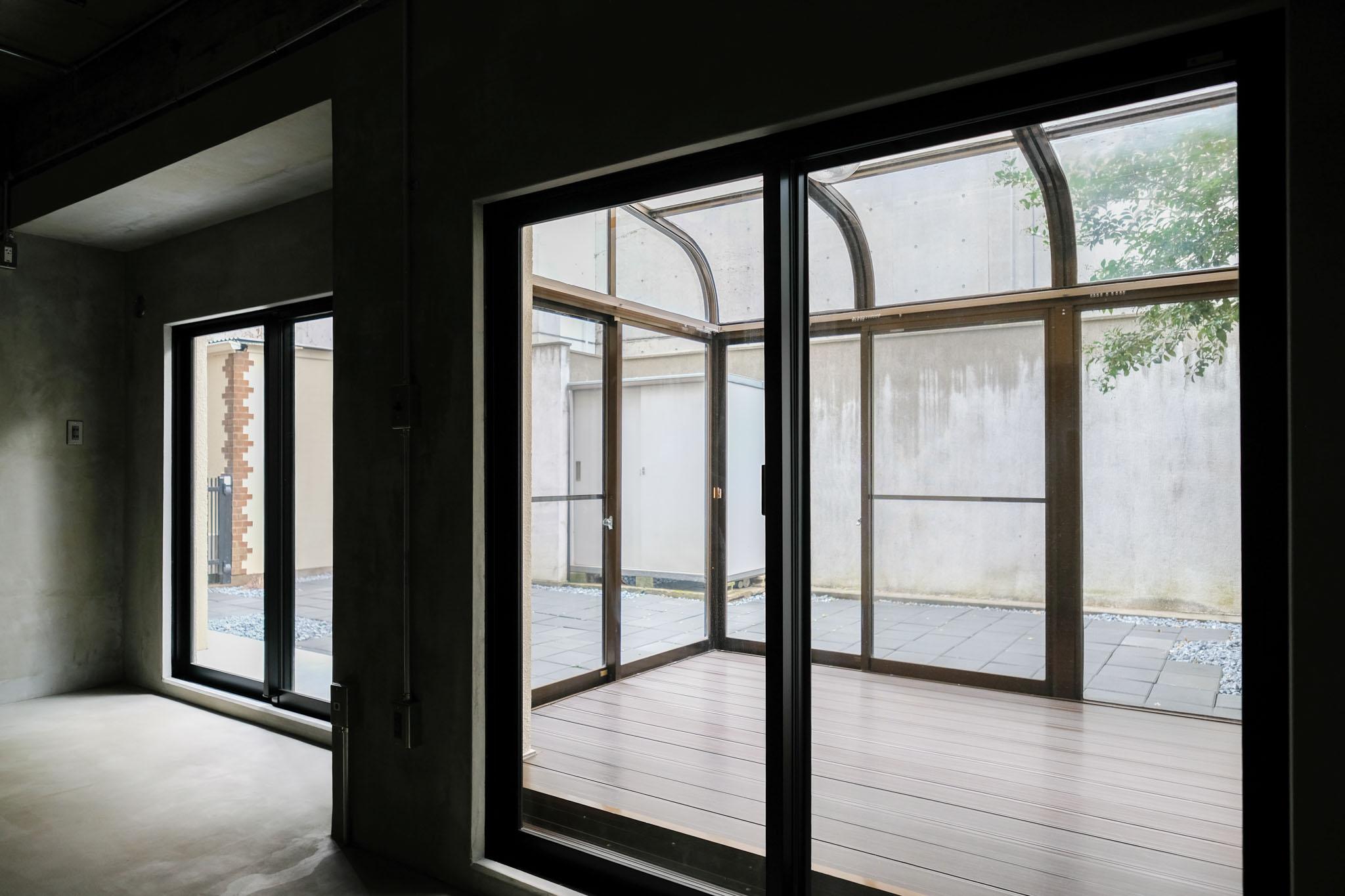 渋谷区神宮前の賃貸物件/室内から見る、アーチ屋根のサンルーム。その奥に平板張りの庭（103号室）