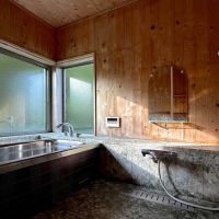 長野県上水内郡信濃町富濃の売買物件/伊豆石があしらわれた浴室。窓の向こうには、夏の深い緑、冬には雪景色。給湯ボイラーは2026年7月に新品へ交換しています
